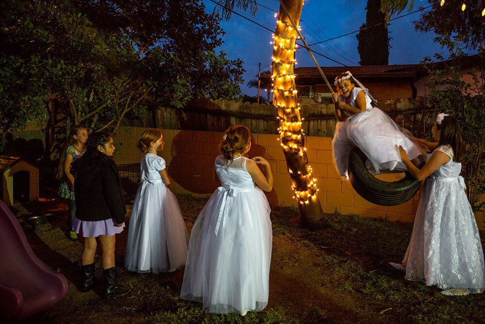 Girls in white dresses play on a tire swing