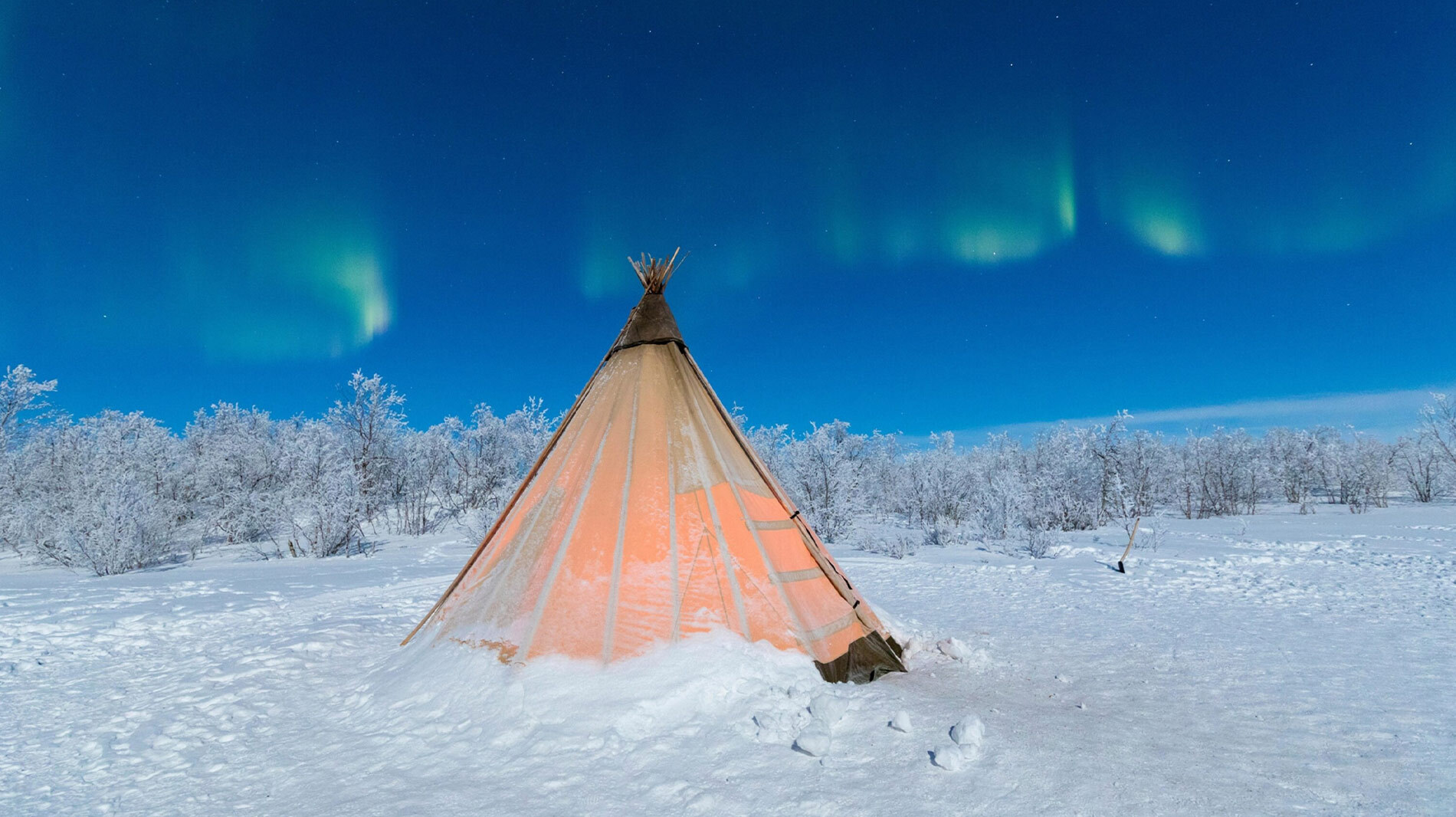 A traditional Sámi tent, called a lavvu, sits under dancing northern lights in Abisko, Swedish Lapland.