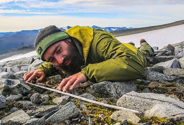 A researcher examines a wooden arrow shaft that emerged from the Langfonne ice patch in Norway. Radiocarbon dating is used to determine the age of many objects once trapped within the now-melting ice.