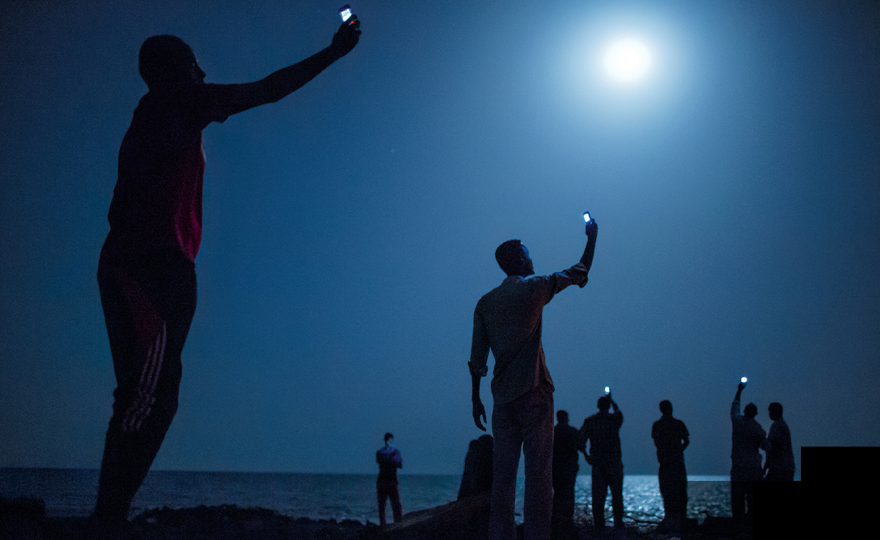 In Djibouti, along the Red Sea shore, people lift their phones towards the moonlight hoping for a mobile signal from neighboring Somalia.