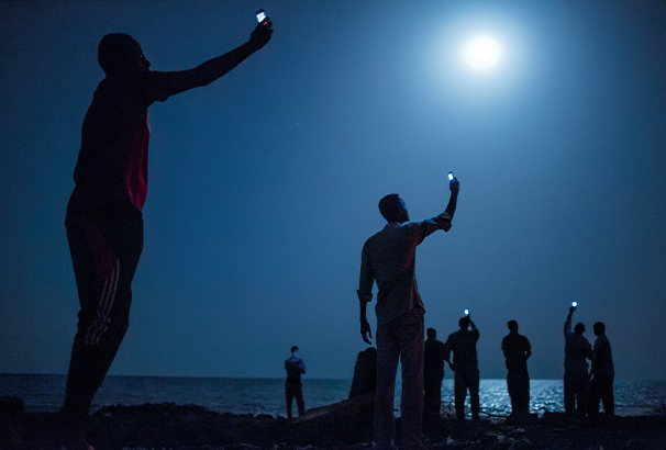 In Djibouti, along the Red Sea shore, people lift their phones towards the moonlight hoping for a mobile signal from neighboring Somalia.