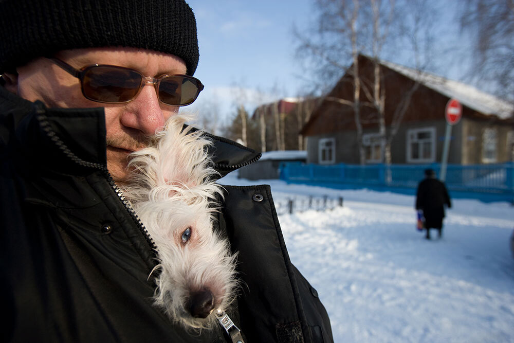 A man holds a white dog inside his coat