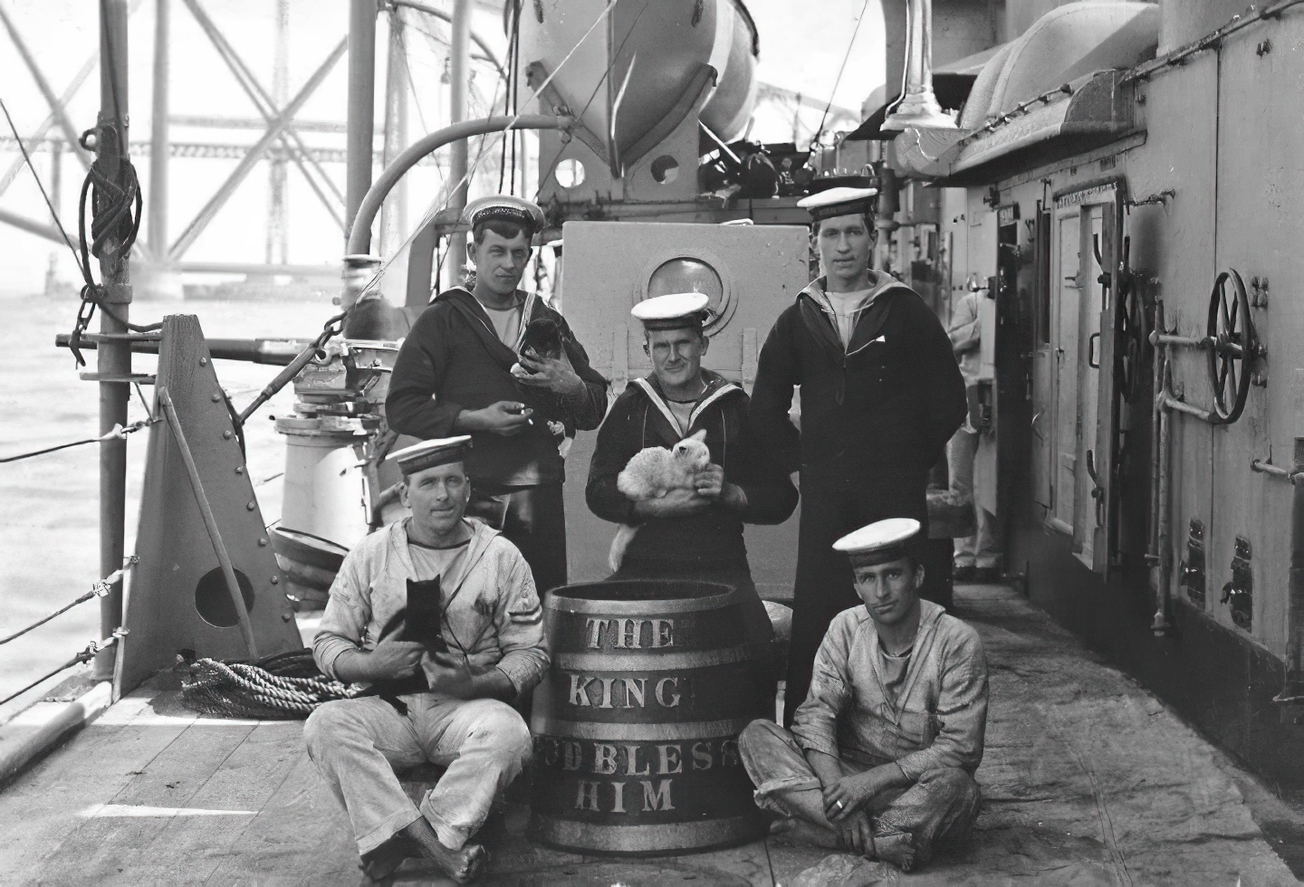 U.K. Royal Navy sailors pose by a rum barrel in 1914 with the ship cats of HMS Sentinel.