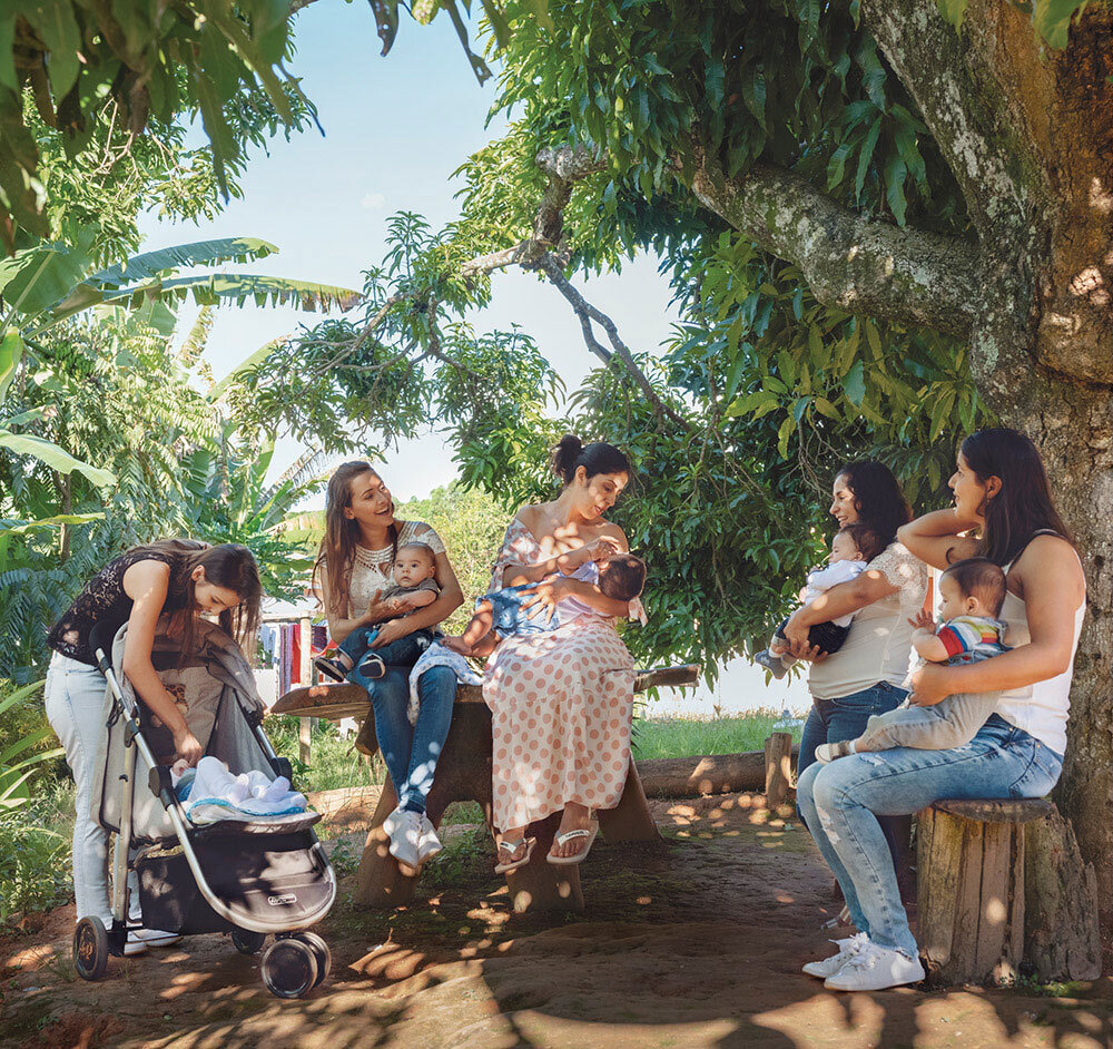 women and their babies sit under a tree