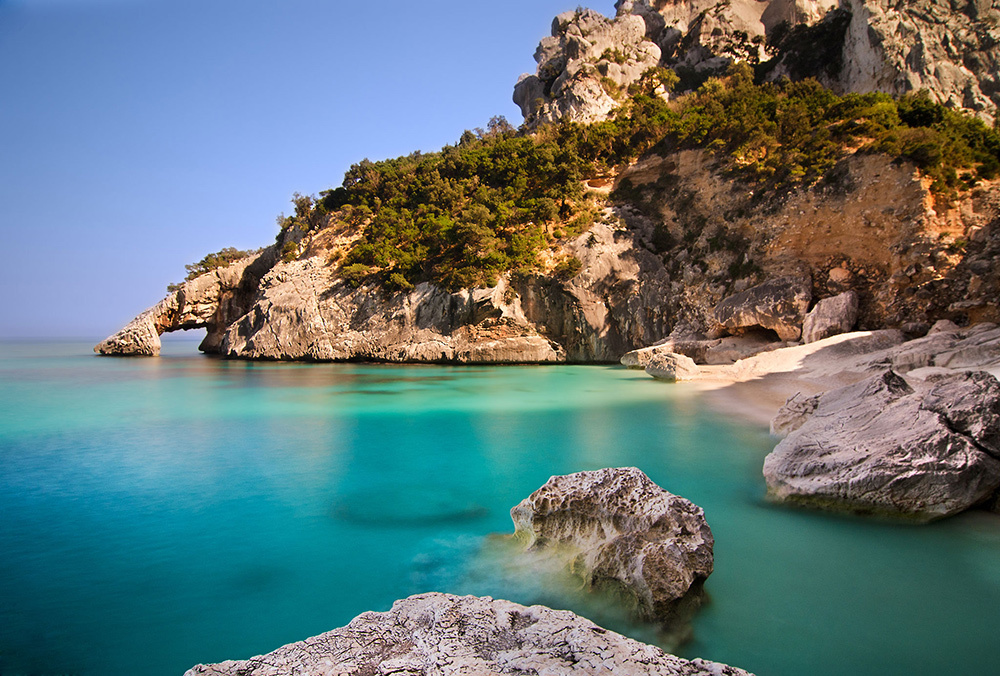 Rock formations next to a small, sandy beach and calm, turquoise blue sea.