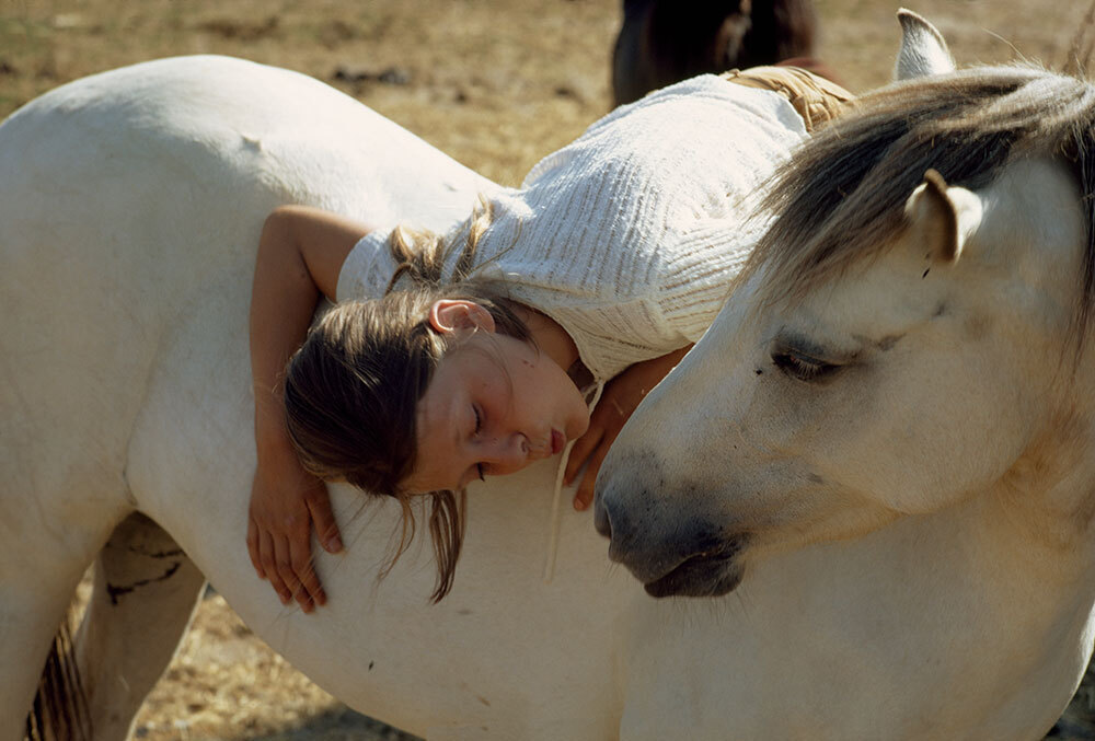 A picture of a girl leaning in to kiss a horse