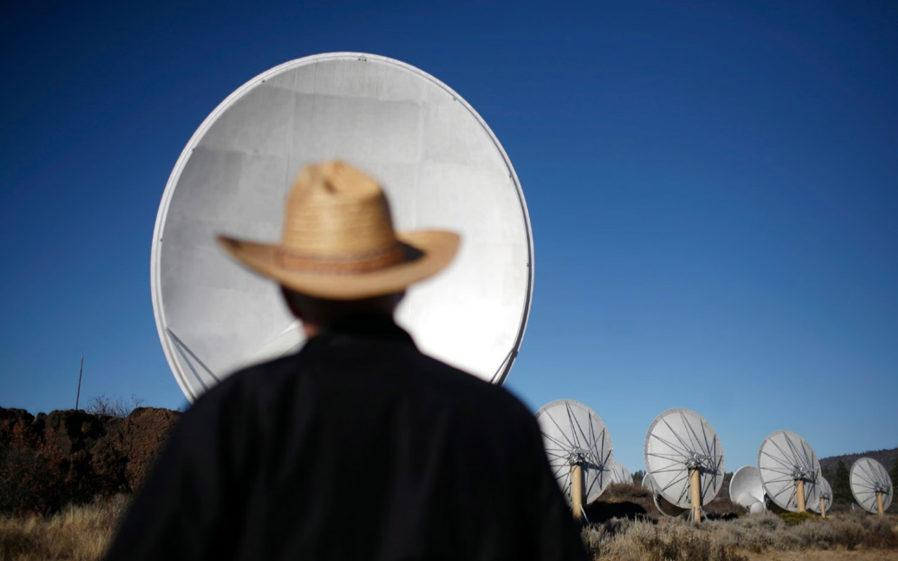 A man in a cowboy hat looking at telescopes.