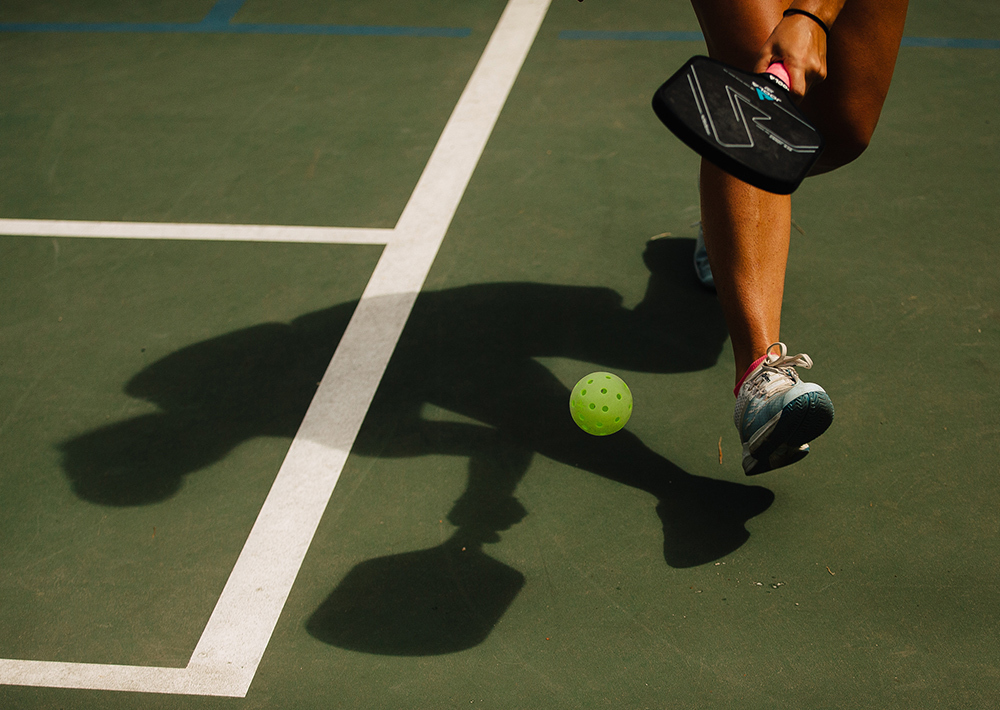 The shadow and legs of a pickelballer chasing down a ball during a match