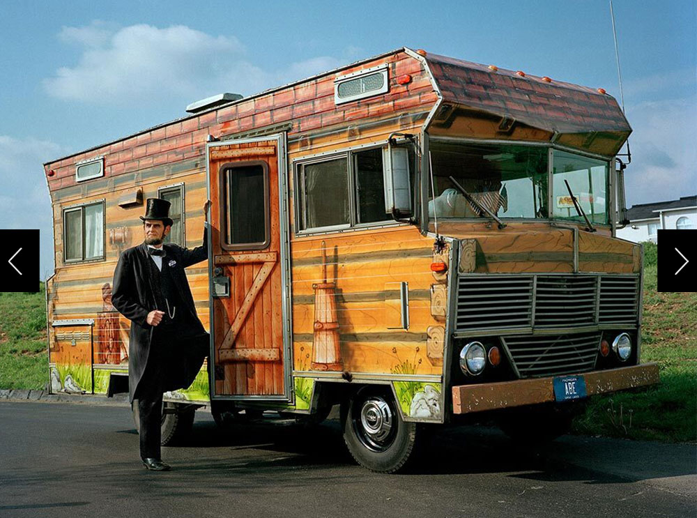 Picture of man dressed like Lincoln standing next to his RV painted like log cabin.