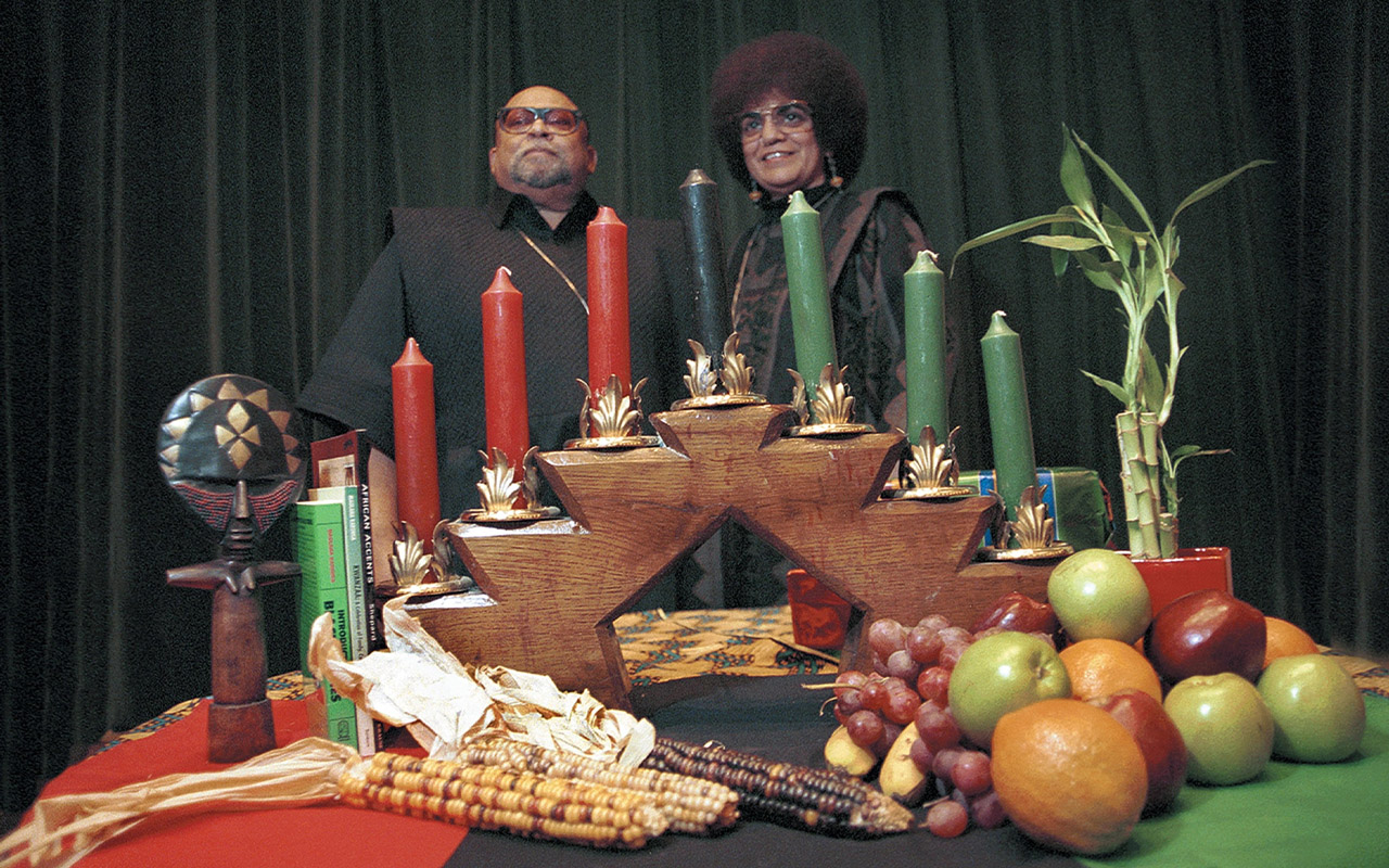 Two people stand behind a table with kwanza candles and food on it