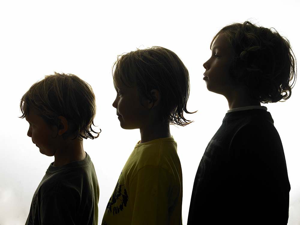 Silhouette of three boys from the side standing in line