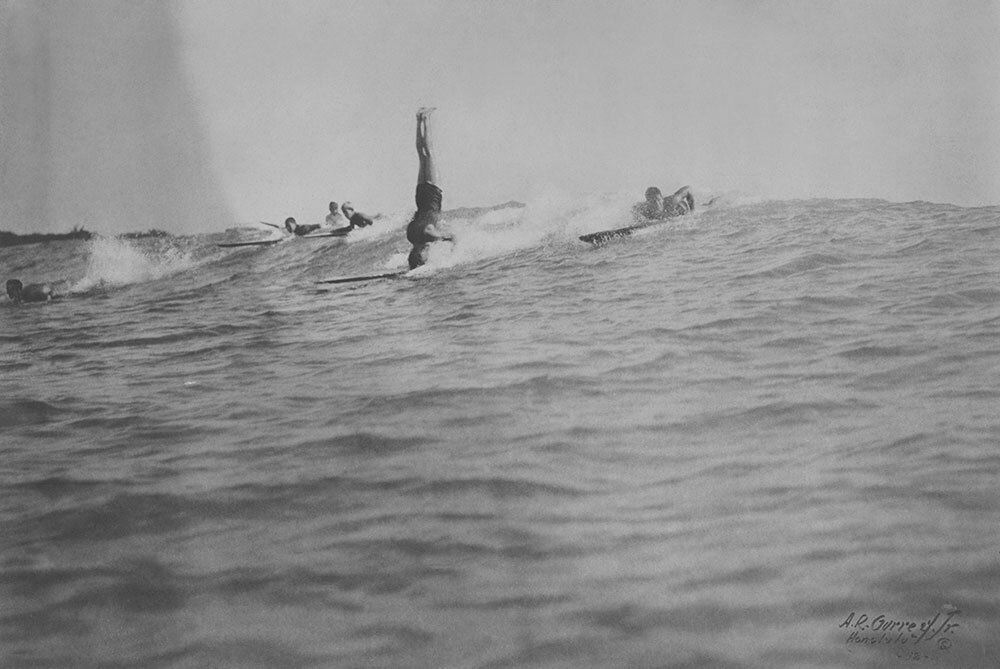 A picture of a man doing a headstand while surfing