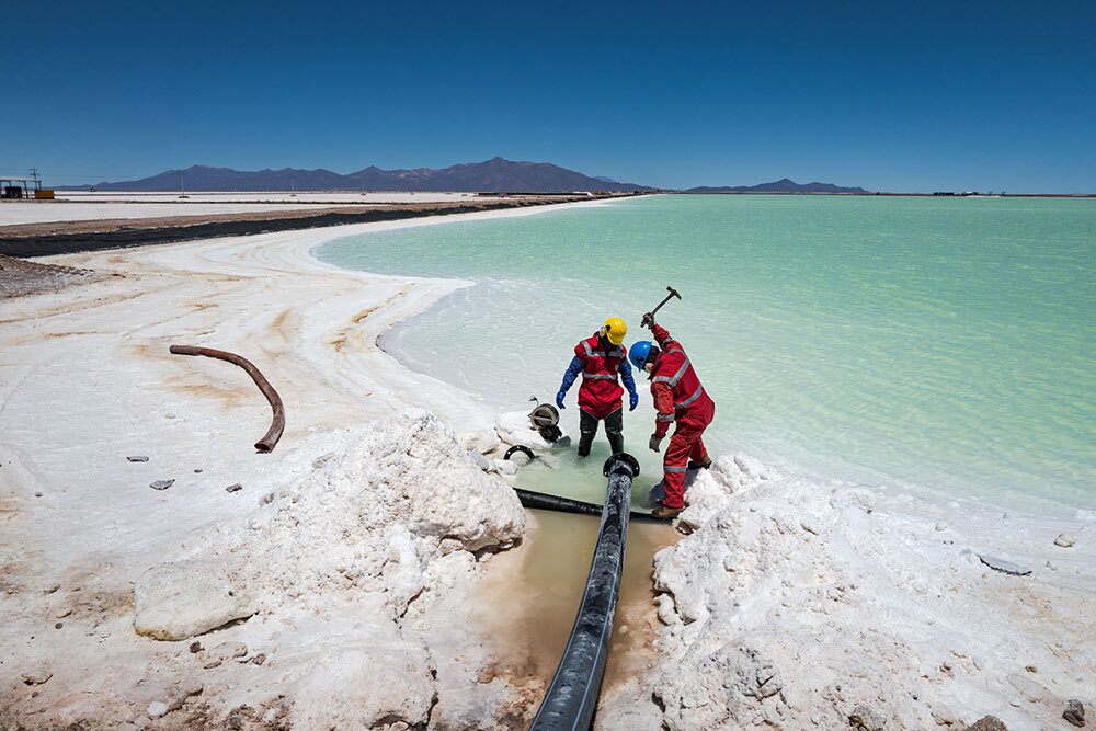 Workers at the lithium pilot plant in Salar use hammers to break up a layer of salt that periodically clogs the pipes transporting brine with lithium into the evaporation pools.