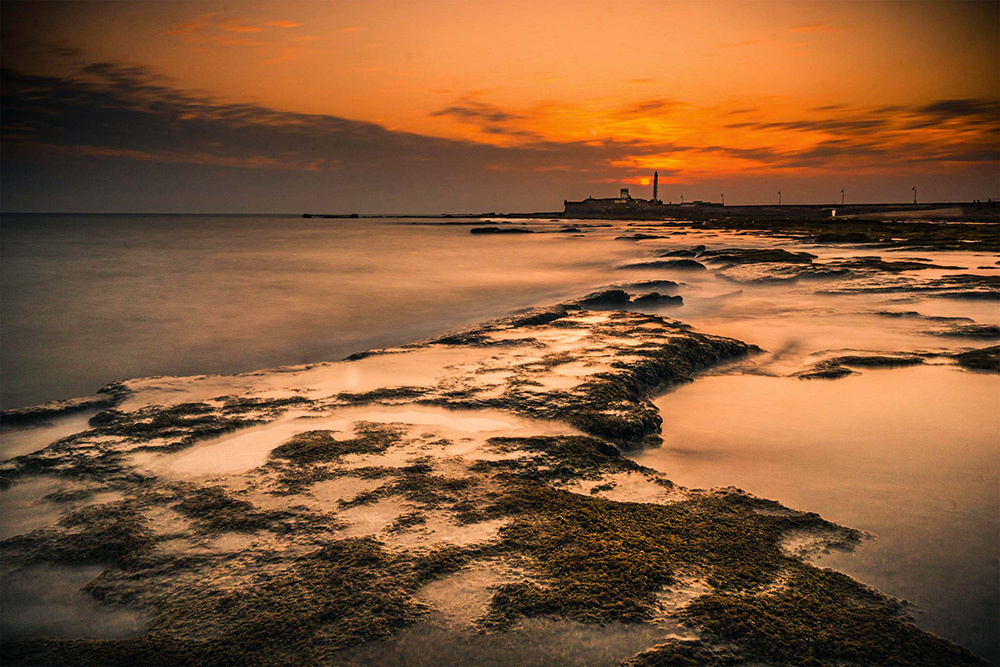 A view of a lighthouse and port at sunset