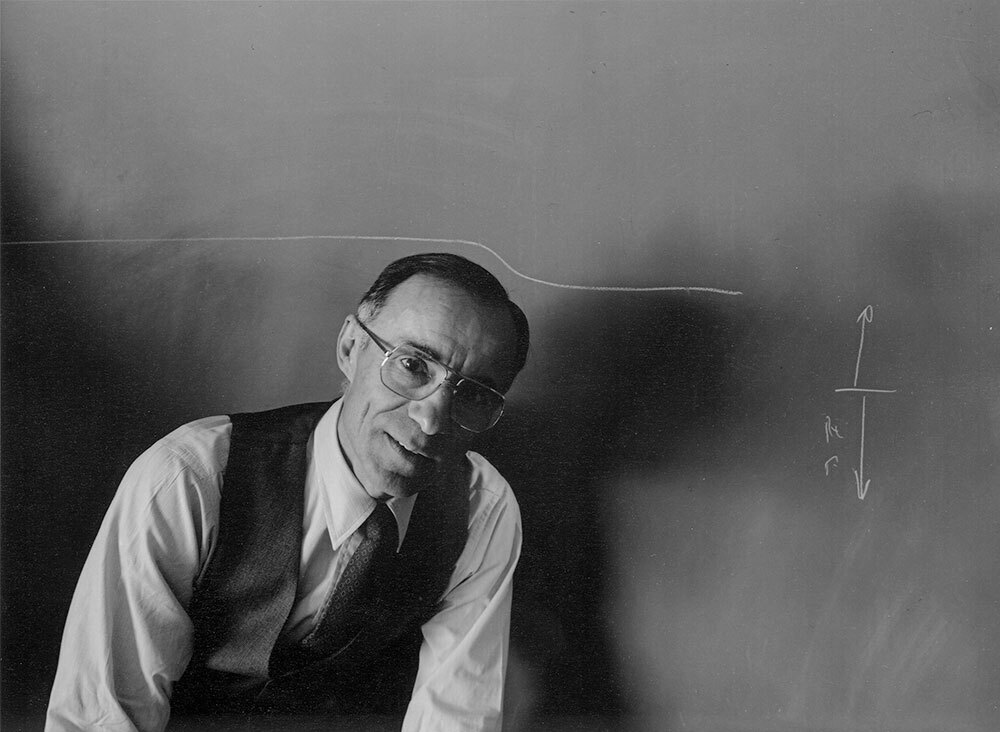 Arno Penzias poses in front of a chalkboard with a formula written on the board