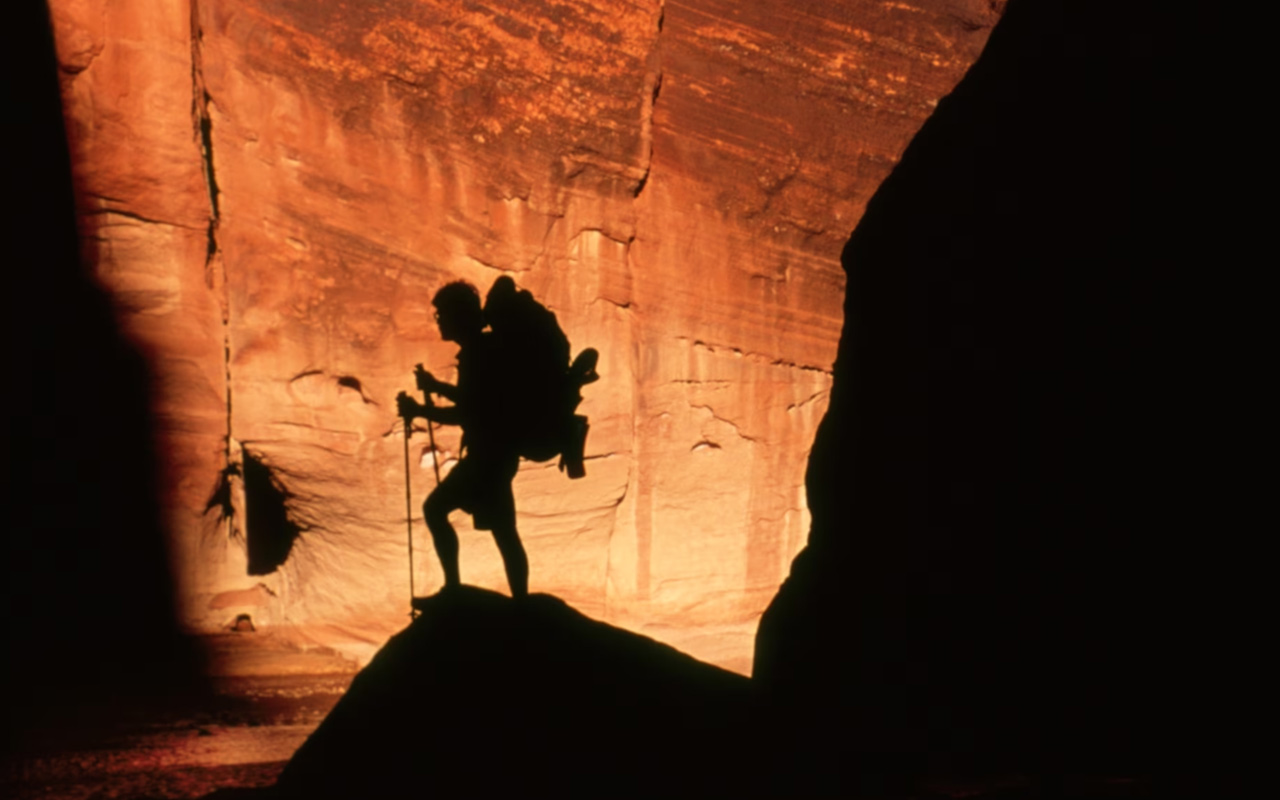 A hiker silhouetted against the orange walls of a slot canyon.