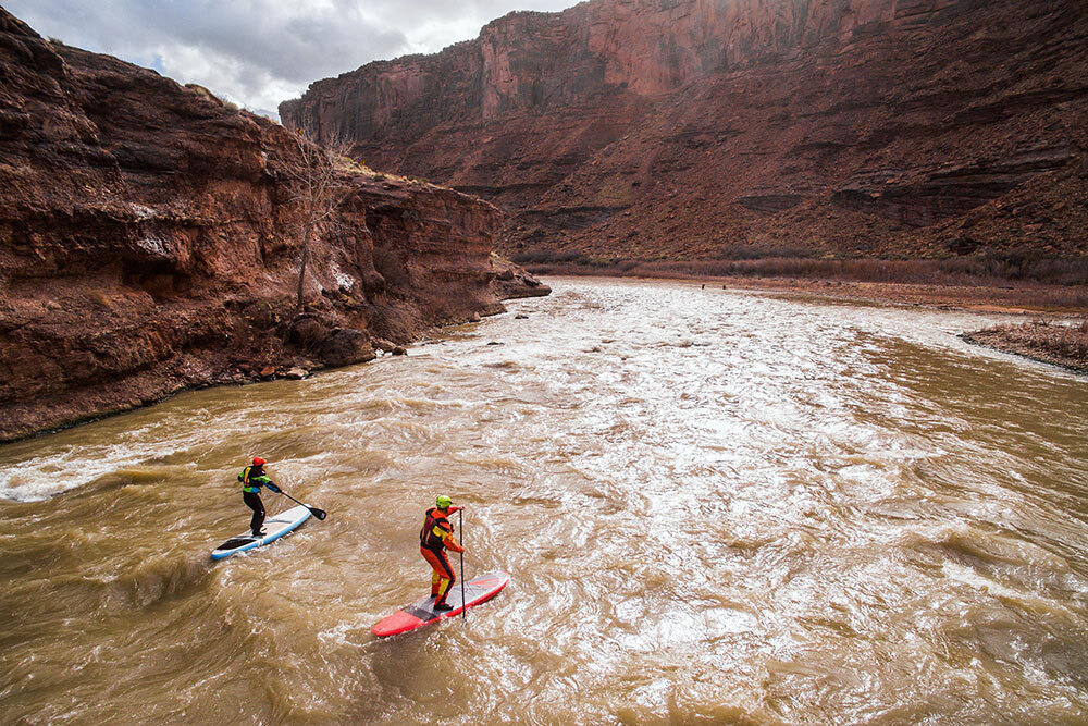 Two stand up paddle boarders navigate a canyon river