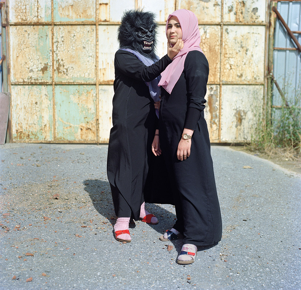 In an Istanbul schoolyard a girl and a friend have fun with a gorilla mask.