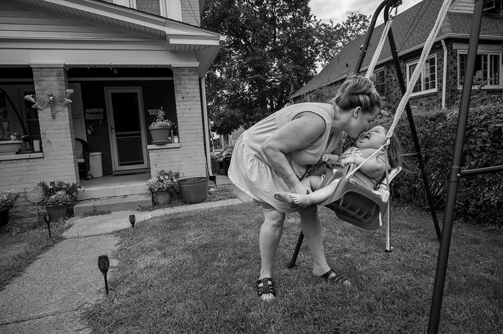 A mother plays with her daughter, who has multiple rare genetic syndromes, on a swing in a front yard