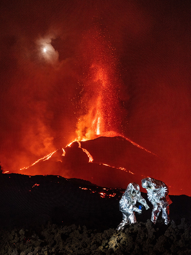 Two people in silver suits stand over a lava slug to take measurements