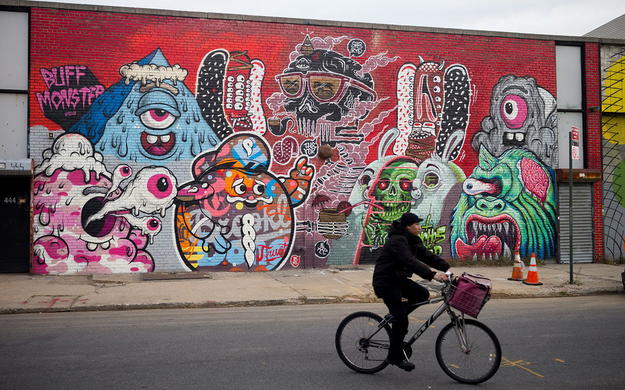 A person in a black jacket on a bicycle rides past a mural.