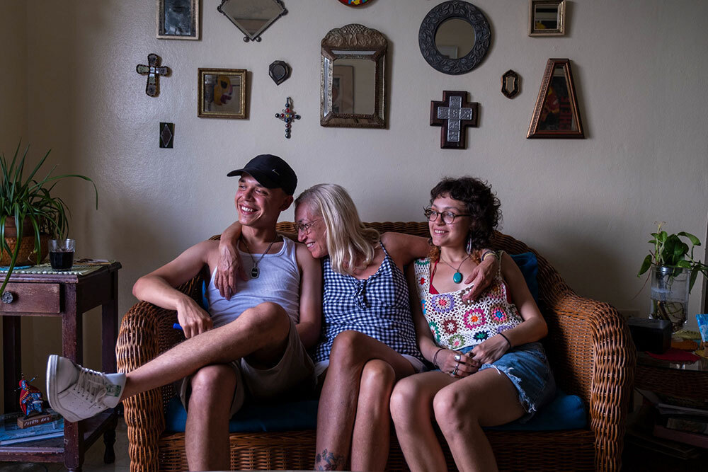 A woman sits on a couch with her arms wrapped around two young adults