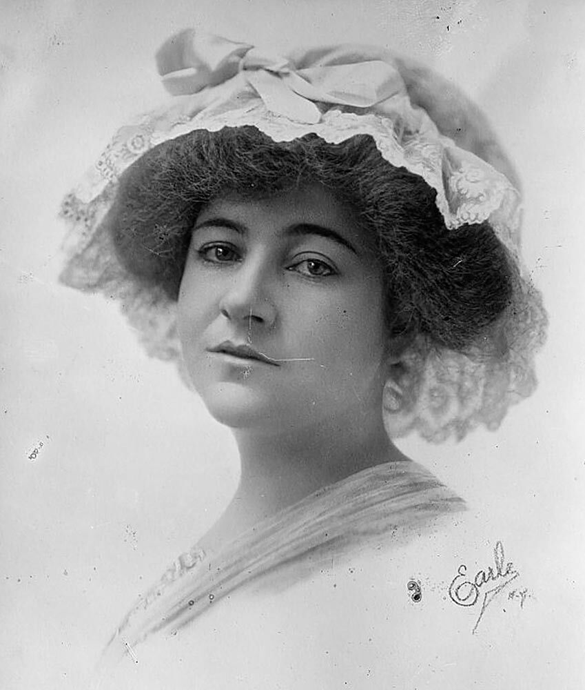 Black and white portrait of a woman from the shoulders up. She is wearing a bonnet with a bow and has short, dark hair.