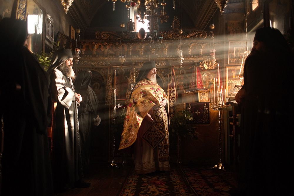 A man in red gold adorned robe stands center frame as light streams