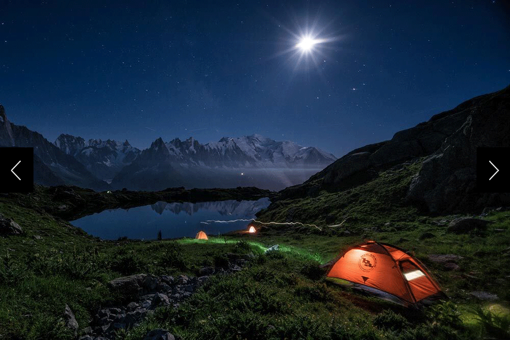 Tents illuminated under headlamp under starry skies in the backcountry of the french alps with a view of the Mont Blanc Massif