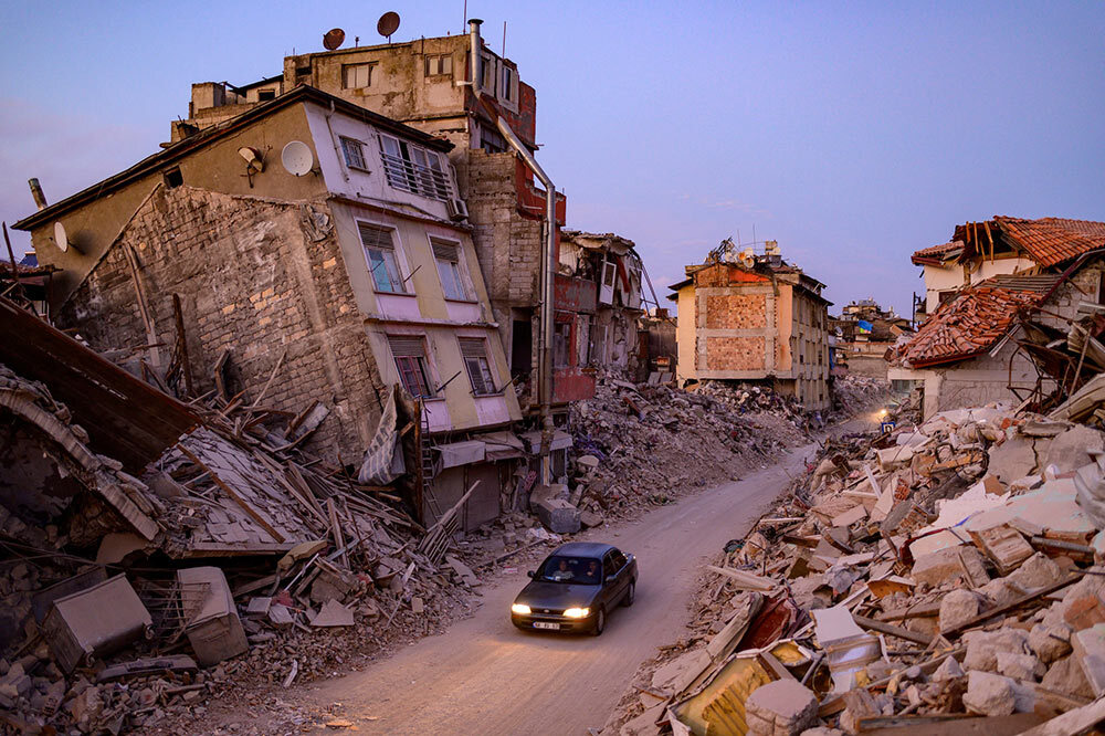 A car drives past collapsed buildings in Antakya, Turkey in February 2023. A 7.8-magnitude earthquake caused widespread destruction in southern Turkey and northern Syria.