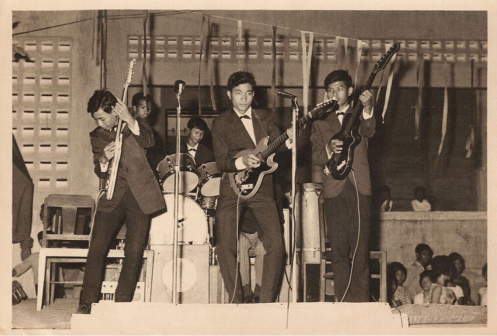 A black and white image of three Cambodian men in a rock band playing guitar on stage