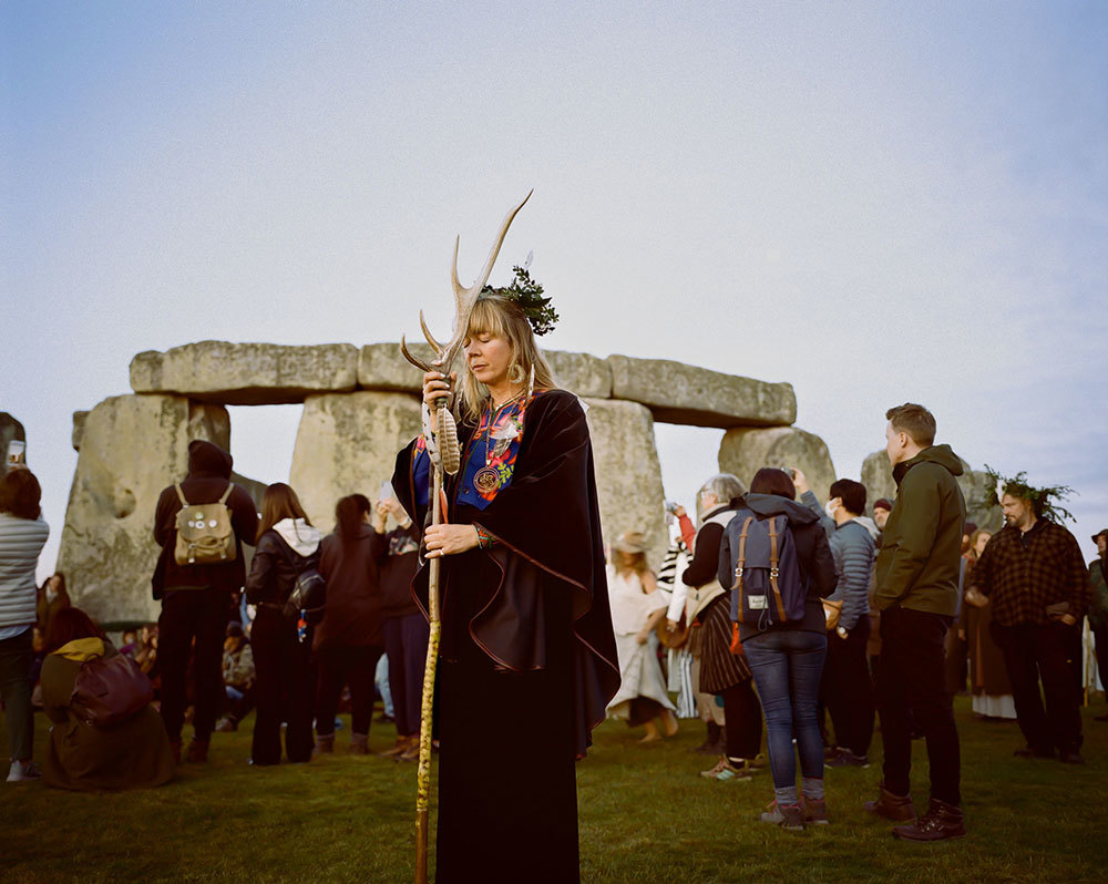 A woman presses a staff to her forehead at Stonehenge