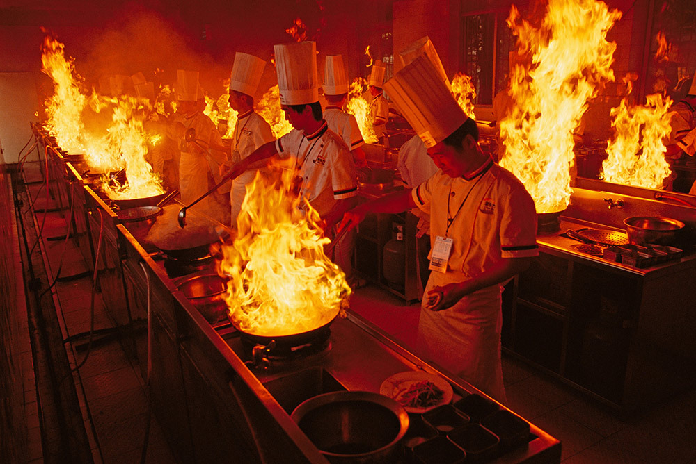 chefs cook vegetables in flaming woks