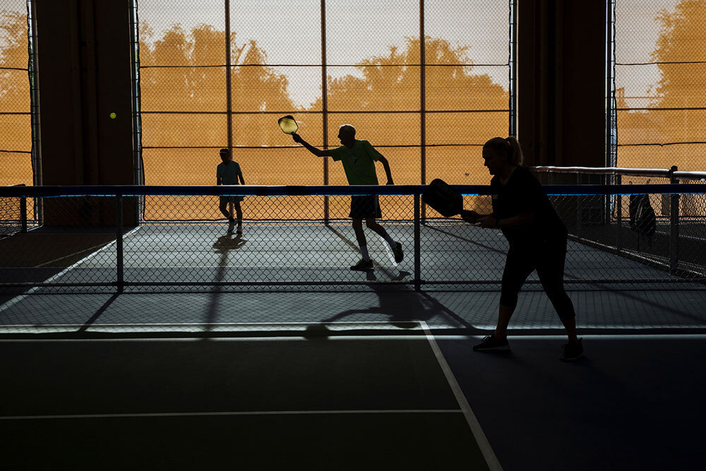 A picture of three silhouetted pickleball players on a court