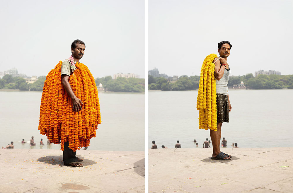 Two men carry long strings of marigolds