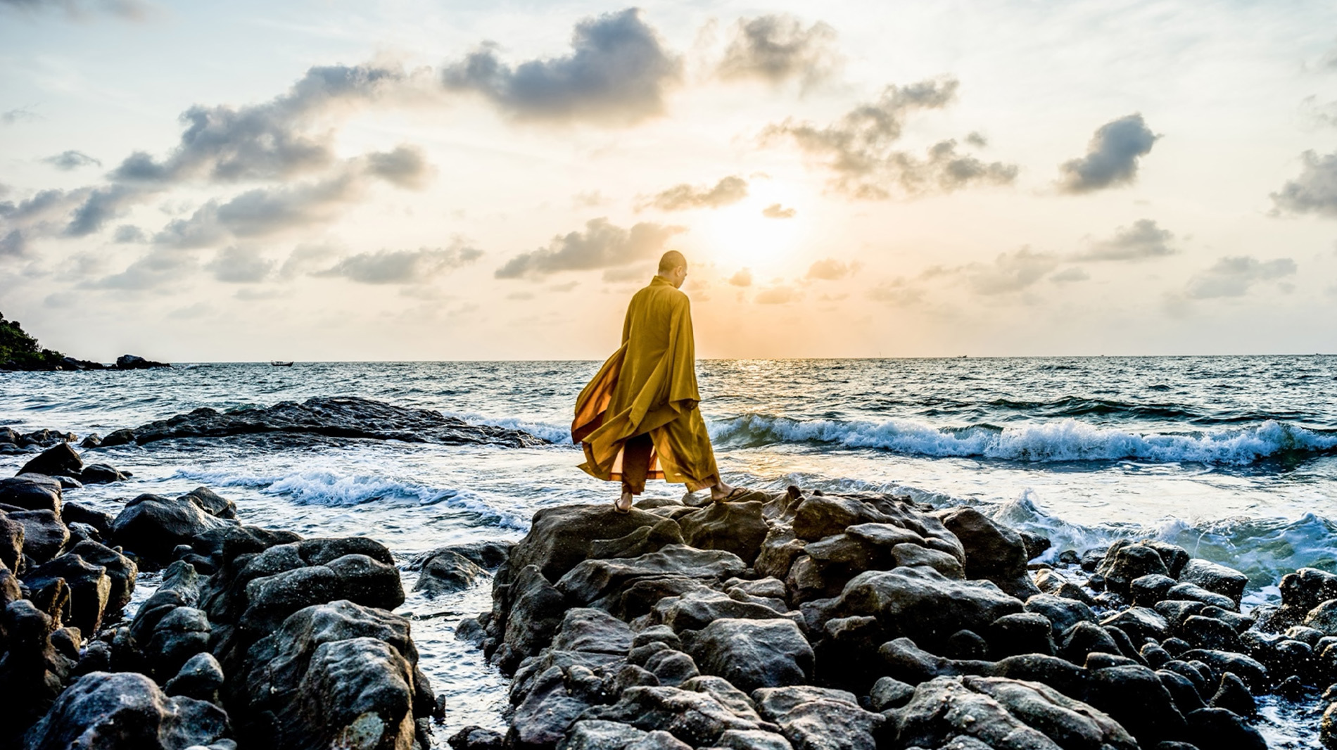 A Buddhist monk meditates at sunrise on the seashore.