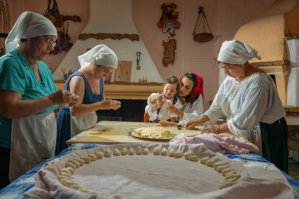 Four women in headscarfs and a child making small round bread rolls