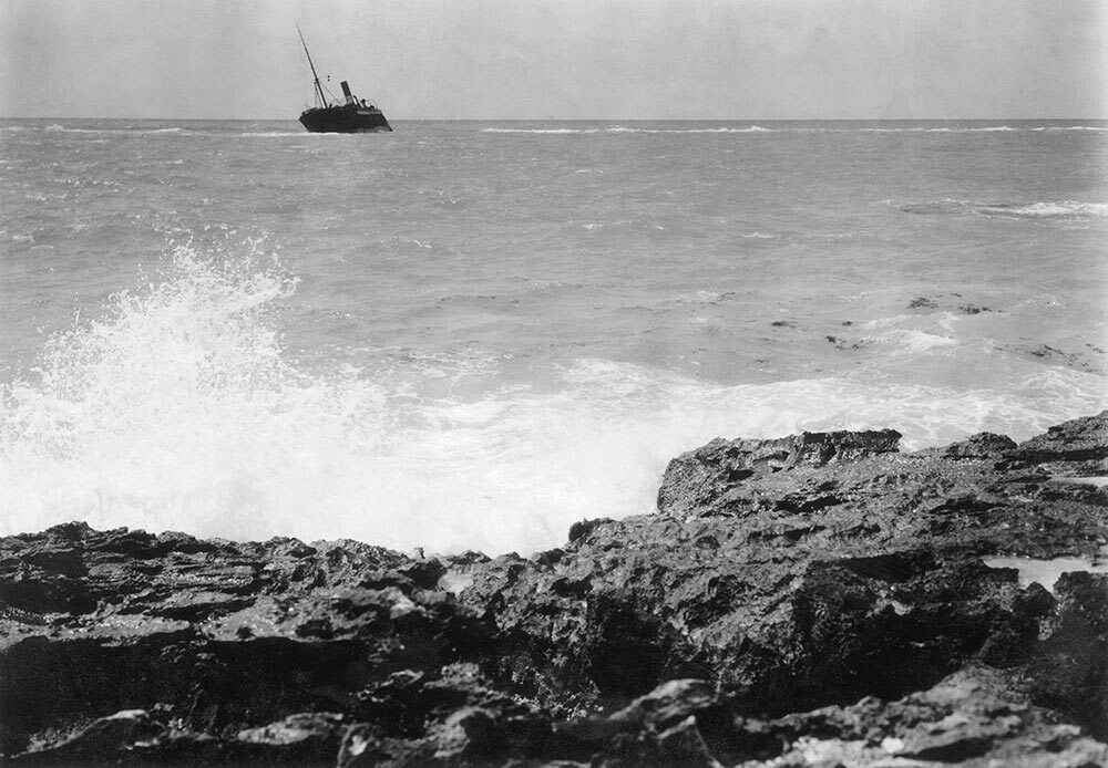 Rocks in the foreground look off in the distance as a ship sinks.