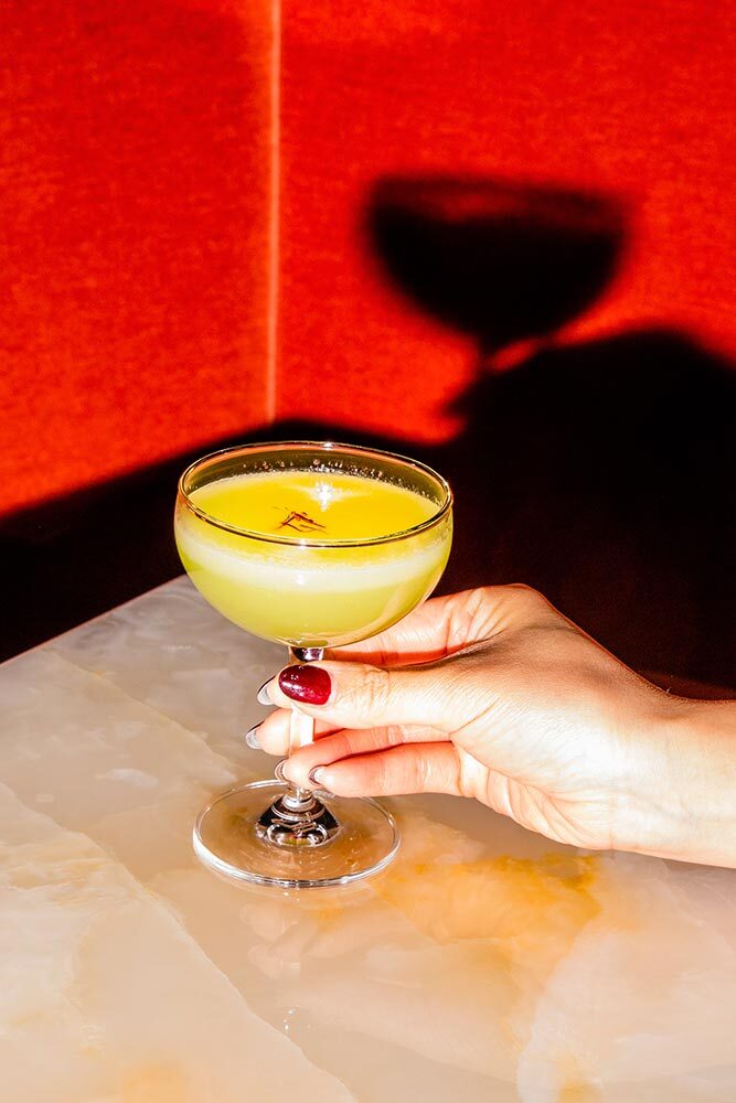 A hand with red nails holding a yellow mocktail.