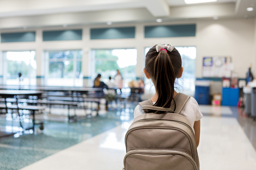 An elementary school girl, seen from behind, pausing as she enters a school cafeteria