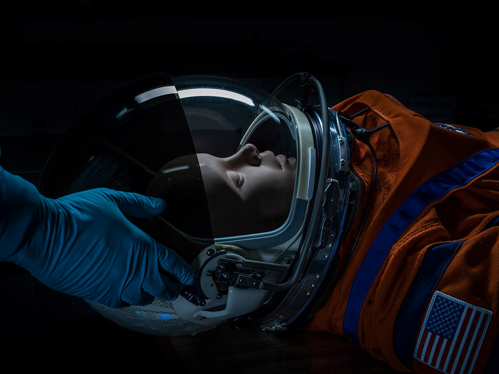 Gloved hands place a space helmet on a mannequin.