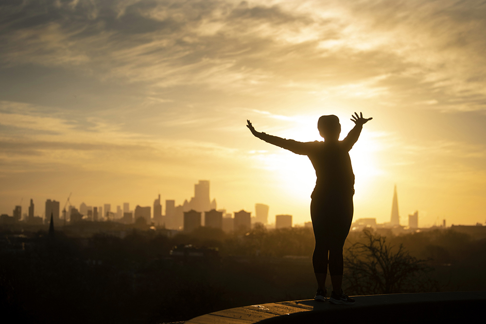 A woman is silhouetted as she performs yoga stretches on Primrose Hill, London, as the sun rises over the city sky.