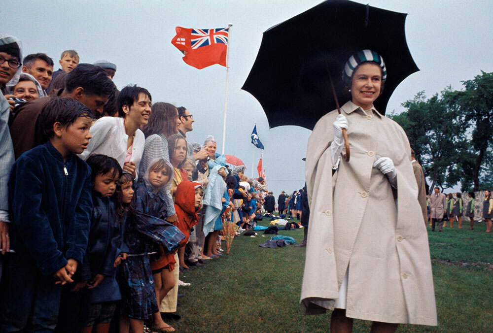 A smiling Queen Elizabeth walks past drenched, smiling Britons in the rain