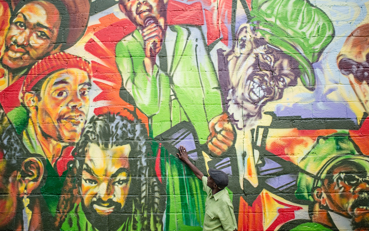 In Toronto’s Little Jamaica, musician Jay Douglas stands in front of the Reggae Lane mural that bears his image.