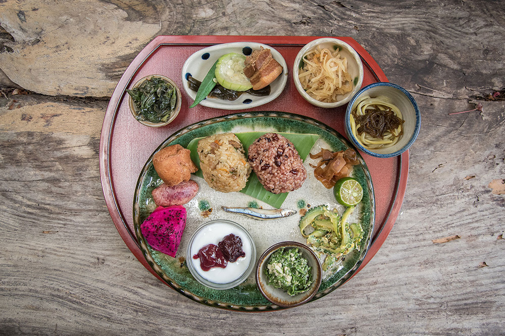 A red plate sitting on wood covered with a variety of different foods, from rice to fruits and vegetables.