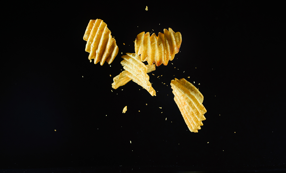 Ruffled potato chips falling, photographed against a black background.