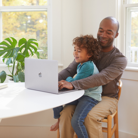 Father and young child smiling and using a laptop computer.