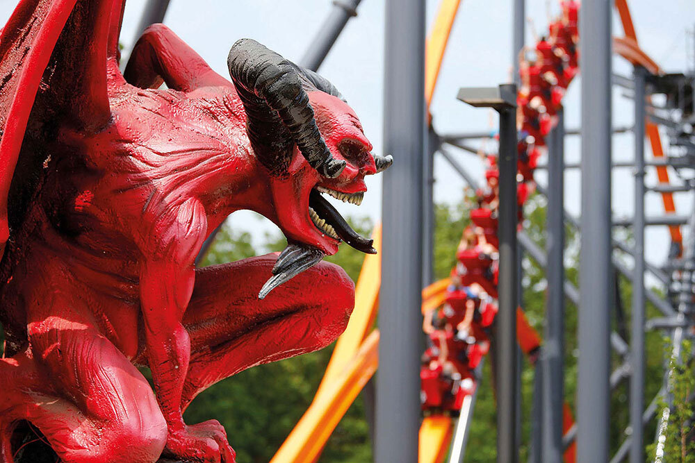 A statue of a devil perches near a roller coaster