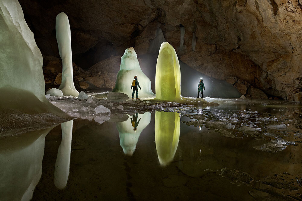 Two people in a cave stand near pillars of ice