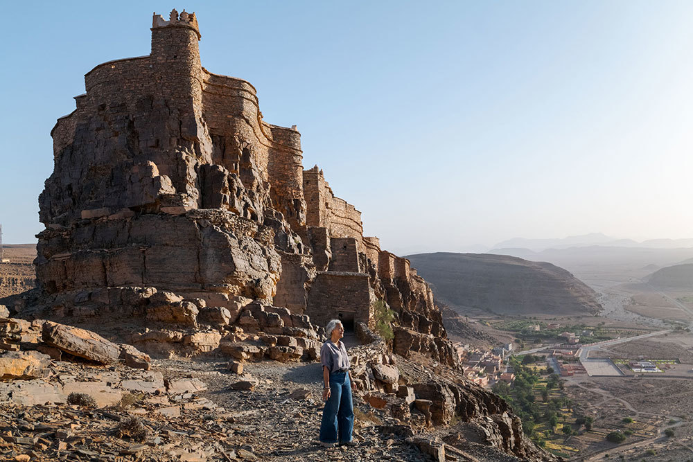 A picture of a woman in front of a large mud brick structure